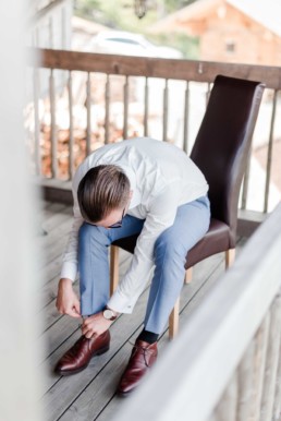 Bräutigam Tom zieht im Hochzeitsanzug seine Anzugschuhe am Hochzeitstag beim getting ready an und wird fotografiert von Hochzeitsfotograf veronika anna fotografie aus München